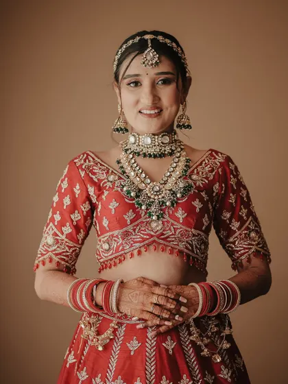 A bright and happy bridal portrait. The bride looks directly at the camera with a warm smile, looking absolutely radiant in her traditional red lehenga and jewelry.