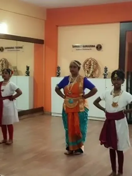 An instructor demonstrates a pose to her Bharatanatyam students, providing direct guidance and correction during a class.