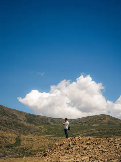 A wide shot showing a lone person photographing the vast landscape of Spiti. This image captures the scale of the mountains and the spirit of a travel photographer.