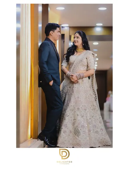 A posed portrait of a couple at their ring ceremony, looking at each other with smiles. The bride's elegant cream lehenga is beautifully captured.