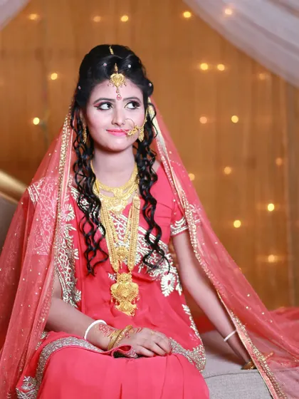 A lovely bridal portrait capturing a candid, thoughtful expression. The soft lighting highlights her intricate gold jewelry and elegant look.
