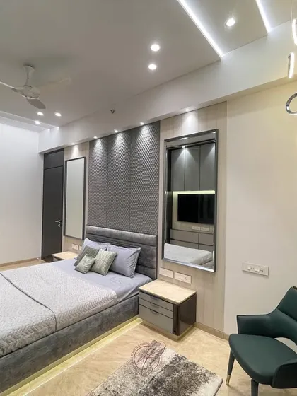 A wide-angle view of the grey bedroom, showing the elegant upholstered bed, integrated wardrobes, and a cozy reading chair. The space is designed to be a grand yet peaceful retreat.