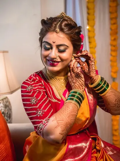 A beautiful shot of the bride getting ready, adjusting her earring with a happy smile. The focus is on the final touches that complete her bridal look.