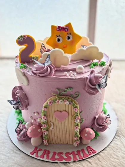 A magical fairy-themed cake for a second birthday. It features a little star character, a fairy door, and whimsical mushrooms and butterflies.
