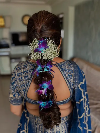 A stunning traditional hairstyle featuring a thick braid adorned with fresh baby's breath and vibrant purple orchids. This is a classic choice for South Indian weddings and ceremonies.