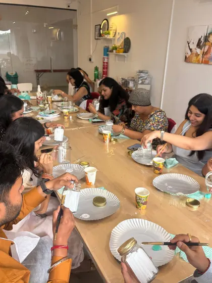 A table full of guests engrossed in decorating jars at a baby shower. It's a lovely way for everyone to contribute to a collective gift for the new baby.