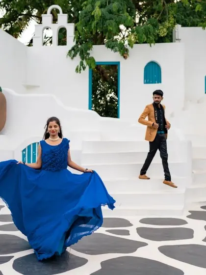 A playful and dynamic shot in a Santorini-themed location. The bride twirls her blue dress while her partner walks down the steps, creating a lively and joyful scene.