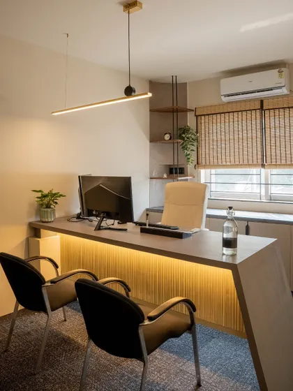 A modern executive cabin with a sleek, minimalist desk featuring under-lighting. Natural materials like bamboo blinds and indoor plants create a calm and focused environment.