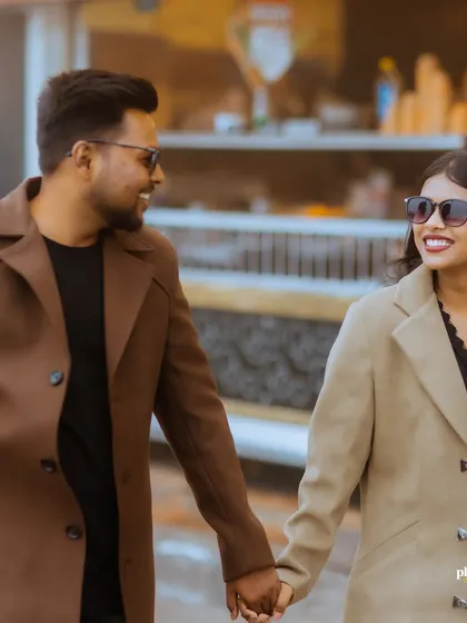 A close-up of a couple holding hands and smiling as they walk, their stylish coats perfect for a chic, urban pre-wedding shoot.