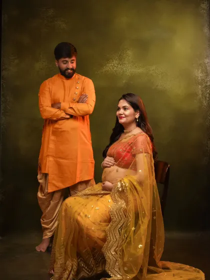 A vibrant couple's portrait with the mom-to-be in a yellow lehenga and the dad-to-be in a matching orange kurta.