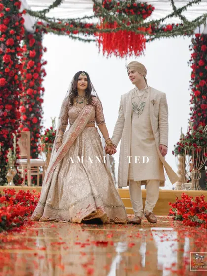 The bride and groom walk hand-in-hand down an aisle of red rose petals after their ceremony.