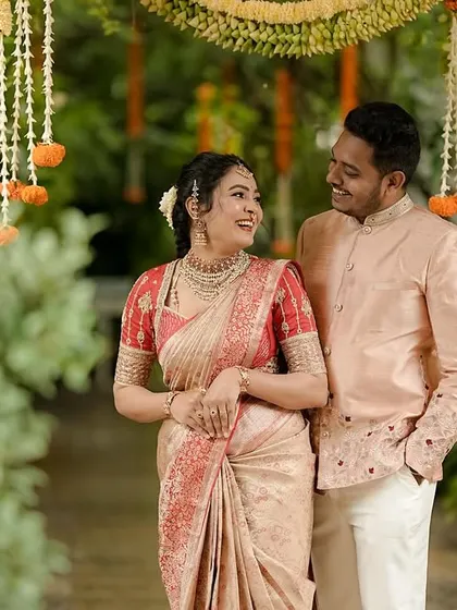 A happy couple enjoying a quiet moment during their celebration. Her beige and red silk saree is perfectly matched with his embroidered peach bandhgala jacket, showcasing our expertise in creating coordinated couple's attire.