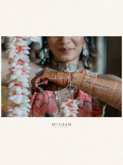 A bride's hand, decorated with mehendi and holding a delicate floral kaleera. This is a quiet, beautiful moment that captures the anticipation and the traditional elements of the pre-wedding ceremonies.