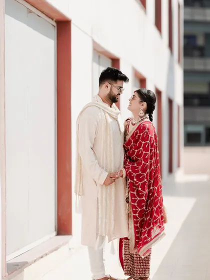 A classic portrait of the couple standing together. The bride's traditional red suit and the groom's white kurta create a timeless and elegant look.