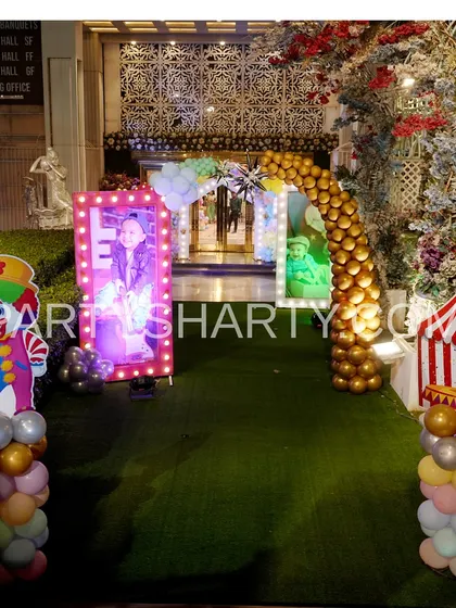 An outdoor carnival entrance with a green turf carpet, clown and circus tent props, and illuminated photo frames for a festive welcome.