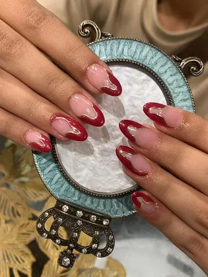 An abstract take on the French manicure, with a deep red "drip" or "wave" design on a clear, almond-shaped nail.