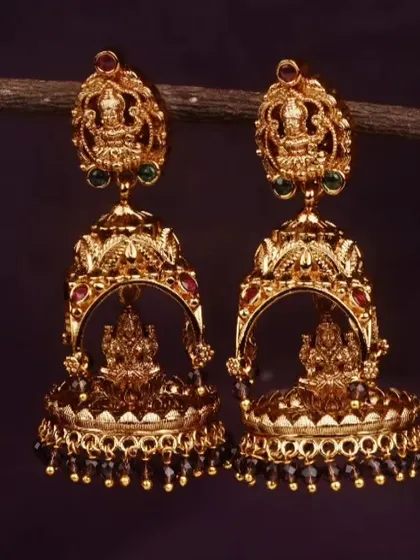 These traditional jhumkis have a beautiful matte gold finish and feature an intricate Lakshmi motif. This pair is detailed with black beads for a classic, elegant look.