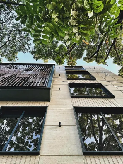 A low-angle view of our mixed-use project, where the modern facade is framed by lush green trees, and their reflections are captured in the windows.