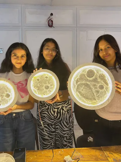 Three participants showcasing their finished moon lamps, each with its own unique texture and glow.