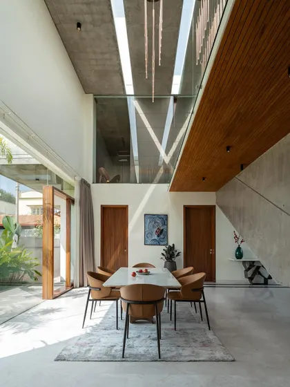 The dining area of The Quarry House, situated next to a large glazed opening and beneath a dramatic, angular concrete staircase.