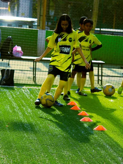 A young girl practices her dribbling through a line of cones. I provide equal opportunities and focused training for my female players to excel.