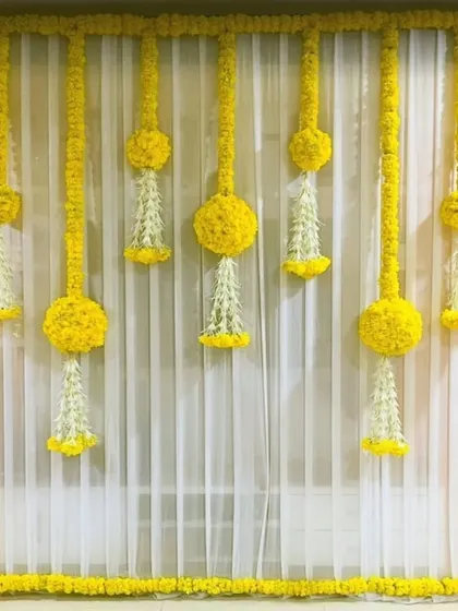 A classic and elegant decor choice for Ganpati or any home puja, featuring bright yellow drapes and traditional floral hangings.