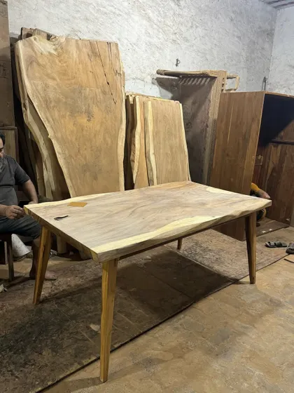 A live-edge table in progress at my workshop, with large wood slabs in the background. This shows the raw material I work with to create these unique pieces.
