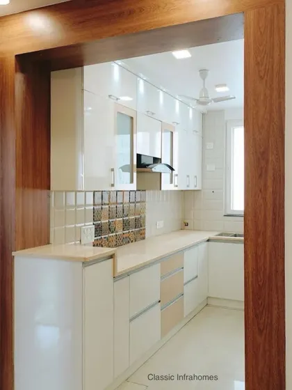 This is a bright and welcoming kitchen we designed for a 3BHK in Great Value Sarnam, Sector 107 Noida. The space is framed by wood-finish laminate, creating a warm contrast with the high-gloss white cabinets. The design includes a breakfast counter for casual meals.