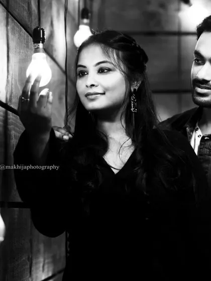 This black and white pre-wedding portrait has a classic, cinematic quality. The focus on the bride's expression as she holds the light bulb adds a touch of artistry and storytelling to the image.