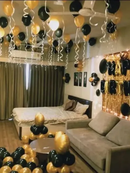 A stylish black and gold themed room decoration for a birthday, with a foil curtain backdrop and balloons filling the space.