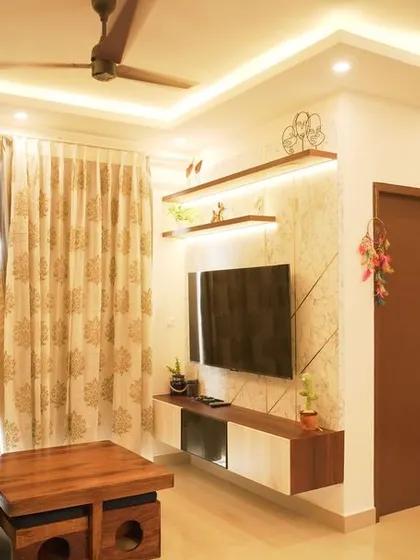 A cozy living room with a dark sofa and a TV unit featuring a textured wallpaper back panel and floating shelves. The warm lighting creates an inviting ambiance.