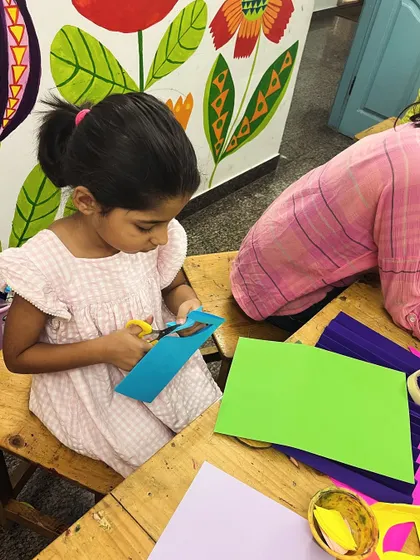 Scissor skills in action! This student is practicing her cutting as she prepares parts for her paper dragon, an important skill for all future crafting.