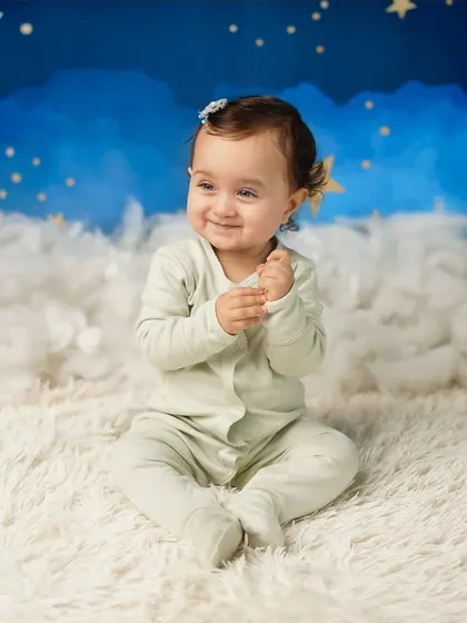 A happy, clapping baby against the dreamy cloud and star background. Her joy is infectious, making for a heartwarming portrait.