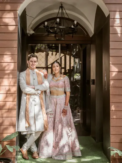 A posed but relaxed portrait of a couple in front of a modern, stylish entryway. Their elegant pastel outfits and confident stance make for a chic and sophisticated wedding photo.