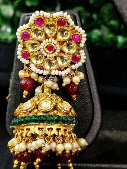 A vibrant jhumka with a floral top made of kundan and pink stones, with a green enamel jhumka drop and red beads.