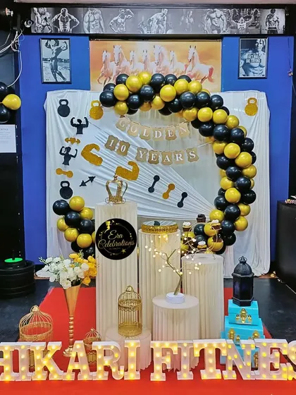 A full view of the gym anniversary celebration setup. The decor includes a balloon arch, themed backdrop, and marquee letters, creating a festive atmosphere right on the gym floor.