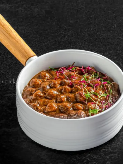 A rich and dark mushroom stew served in a modern white bowl with a wooden handle, shot against a black background.
