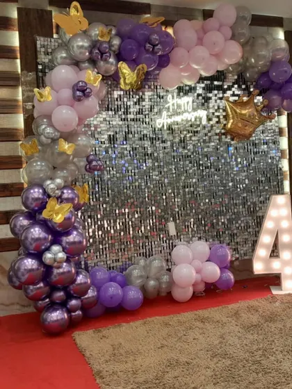 This image captures the beautiful details of the anniversary decor, from the chrome purple balloons to the delicate golden butterflies scattered throughout the arch.