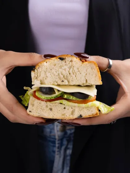 A simple, appealing shot of a sandwich held in two hands, focusing on the fresh layers of vegetables and cheese.