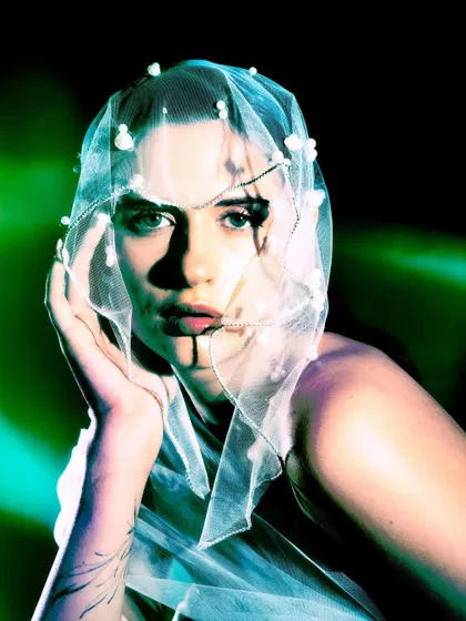 A close-up portrait from the 'Whispering Veil' series, with the model's face partially covered by a delicate, pearl-adorned veil. The green lighting creates a mysterious, underwater feel.