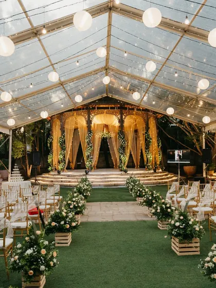 A reception held in a transparent marquee, allowing guests to dine and dance under the stars. The golden Tiffany chairs and white floral aisle runners add a touch of classic elegance.