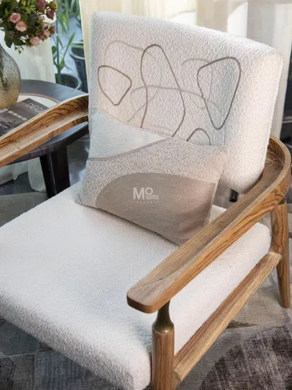 Our Grainline armchair, crafted from premium solid teak wood with visible grain detailing. The frame features brass-toned accents for a touch of vintage elegance, while the bouclé upholstery is adorned with abstract, earth-toned embroidery.