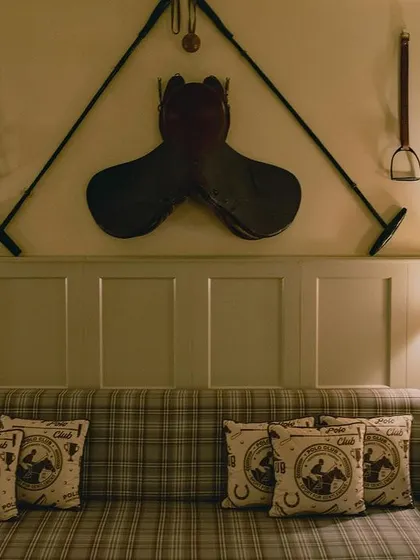 A detail shot of the equestrian-themed decor in the Polo Lounge. A vintage saddle and polo mallets are mounted on the wall, serving as authentic decorative pieces that tell the story of the bar's theme.