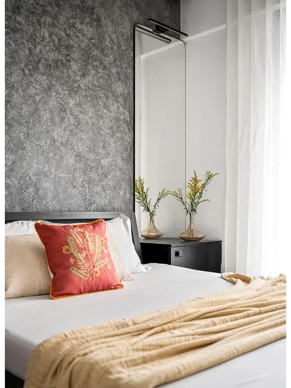 A pop of color from an embroidered cushion adds warmth and personality to the minimalist master bedroom in the 'Nordic Grey Apartment'.