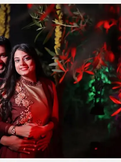 A warm, intimate couple portrait against a backdrop of glowing red flowers. The lighting creates a romantic and cozy atmosphere, perfect for a reception shoot.