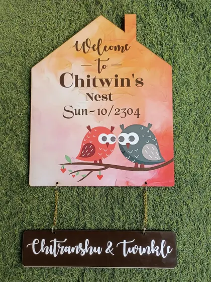 A cute, hut-shaped nameplate for 'Chitwin's Nest,' featuring two owls. The names of the couple hang below on a separate wooden plaque.