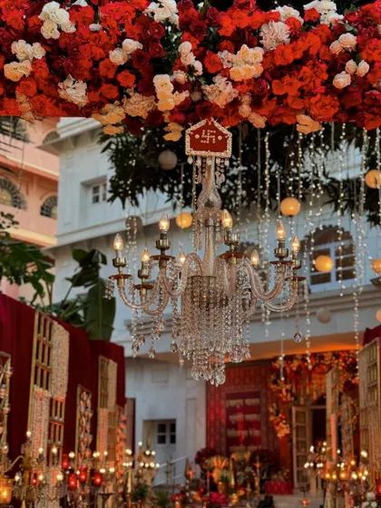 A close-up of a crystal chandelier hanging amidst a canopy of red and white flowers, with a sacred Swastika symbol, blending auspicious tradition with luxurious design.