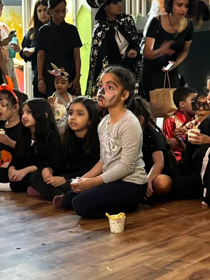 A captivated audience of little skeletons, witches, and ghouls watching a performance. Parents stand in the background, capturing the happy memories on their phones.
