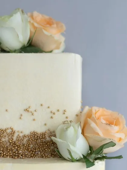 A detailed view of the fresh roses and golden pearl accents on the square wedding cake, showing the simple yet sophisticated design.