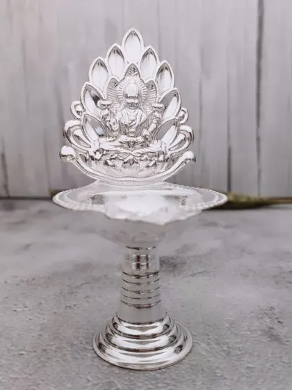 A simple yet elegant German silver diya with a lotus backplate featuring Goddess Lakshmi. It's a beautiful piece for your daily pooja.